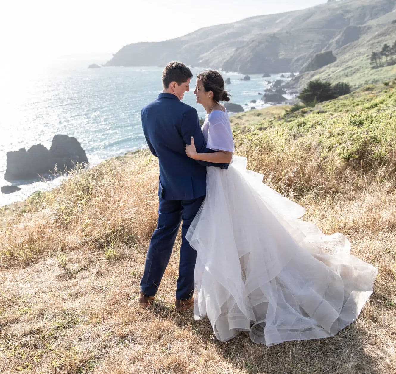Bride and groom on a bluff above the sea, her train spread across the grass