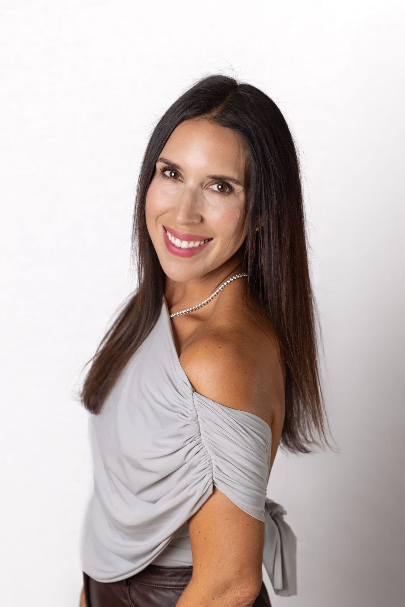 Studio headshot of a woman in a one-shouldered top and pearl necklace