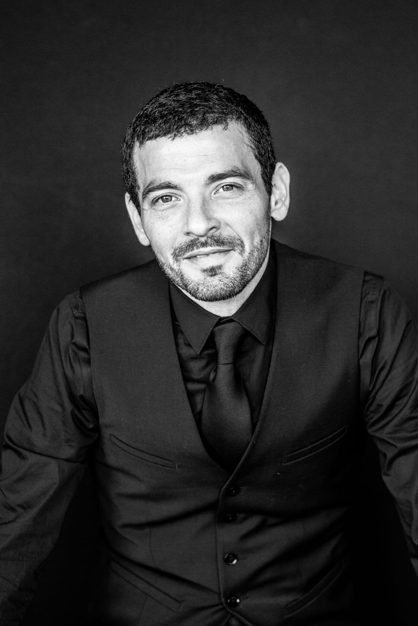 Black-and-white studio headshot of a man in a three-piece suit and tie