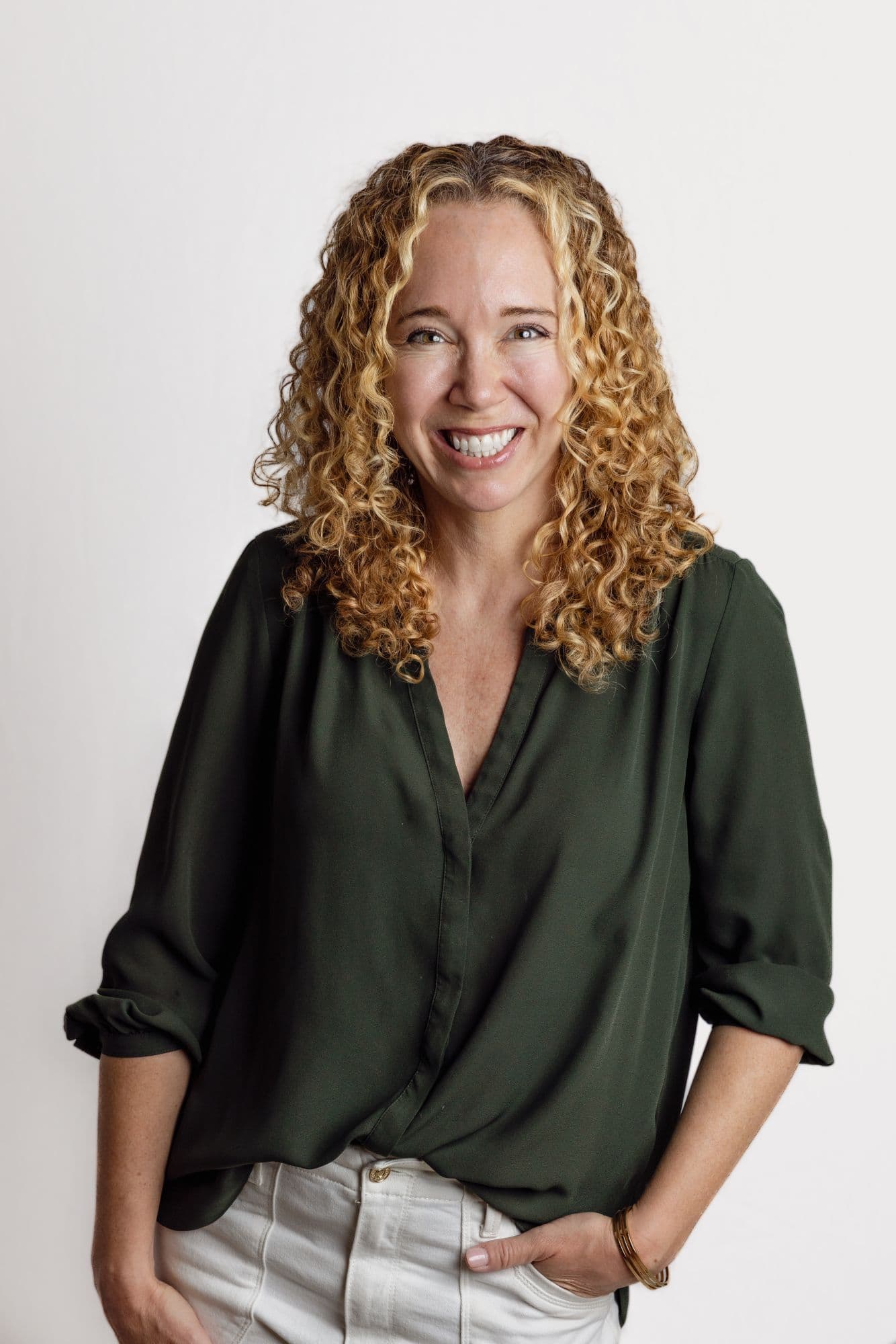 Studio headshot of a woman with curly hair in an olive blouse