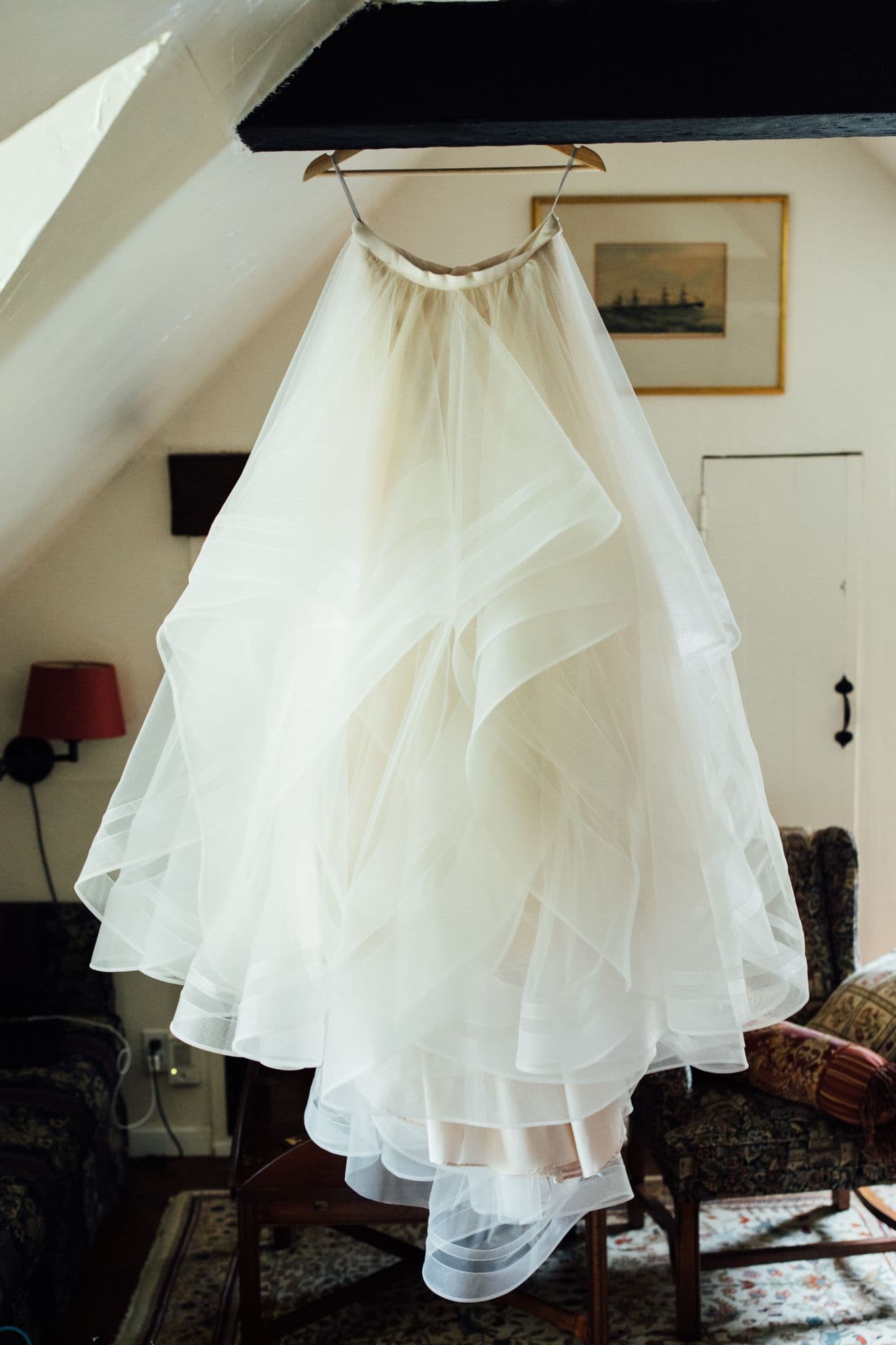 Tulle wedding gown hanging from a beam in a sunlit cottage bedroom