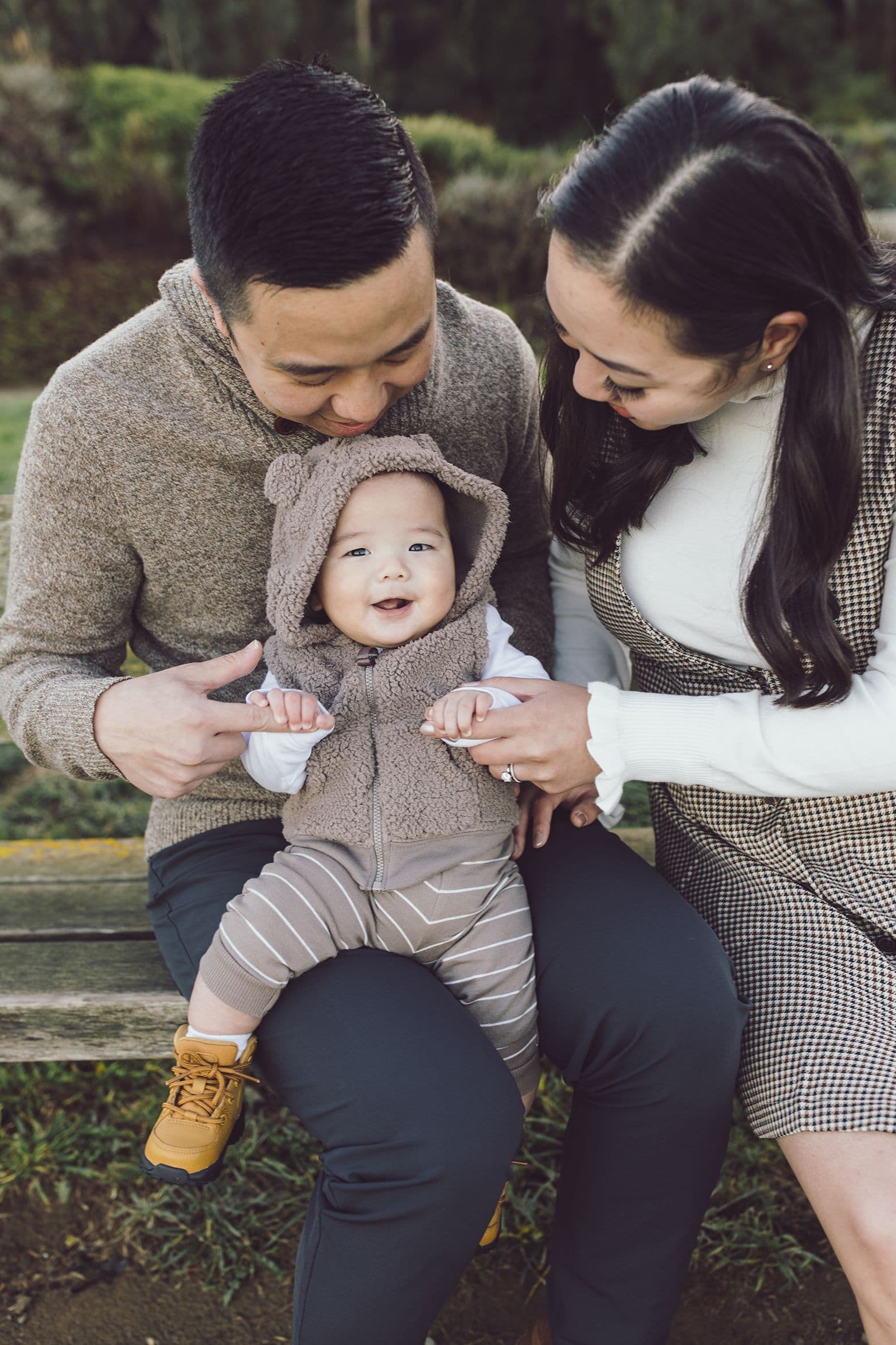 Parents on a park bench with their baby between them, all three mid-laugh