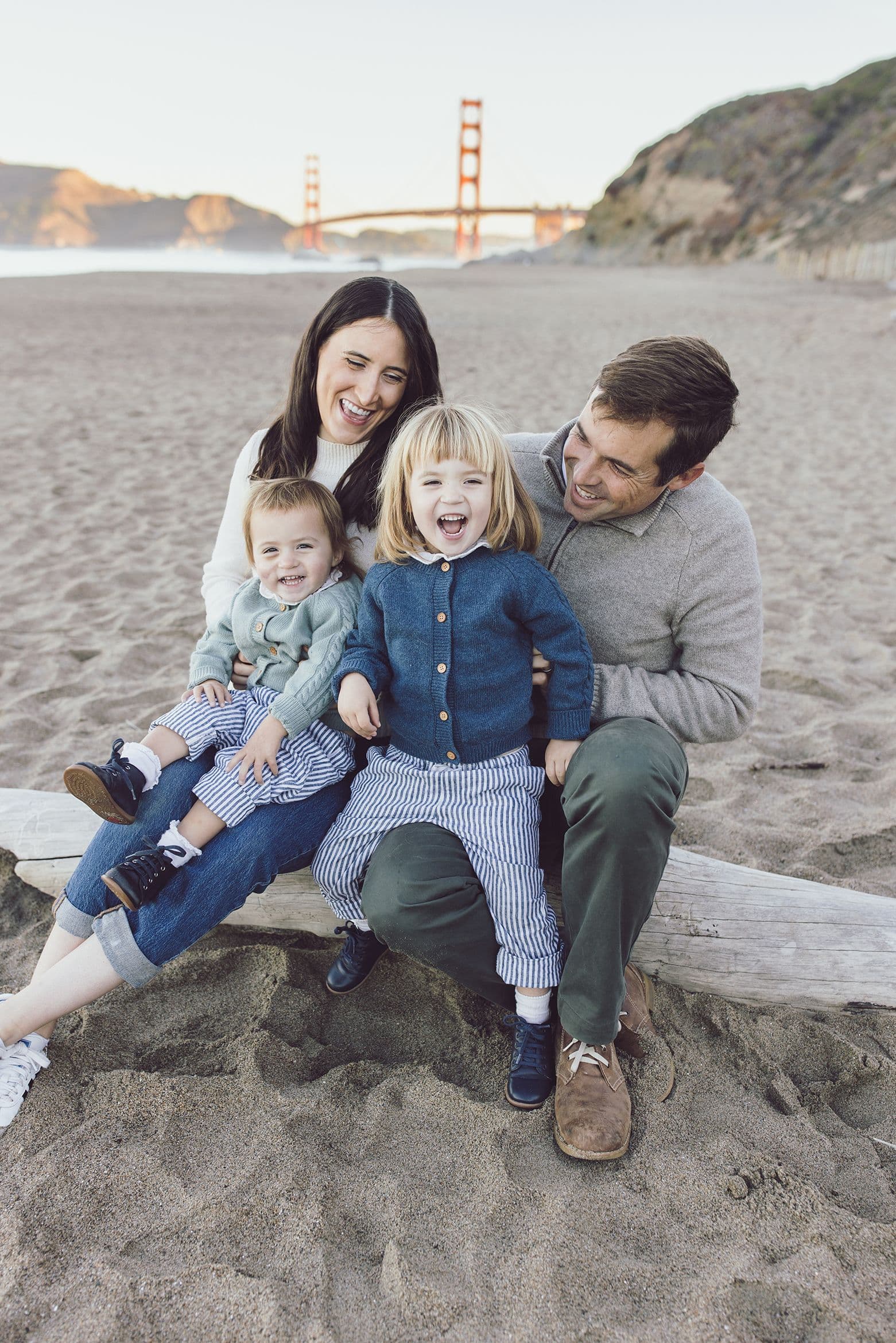 Parents and two small children on a driftwood log at Baker Beach