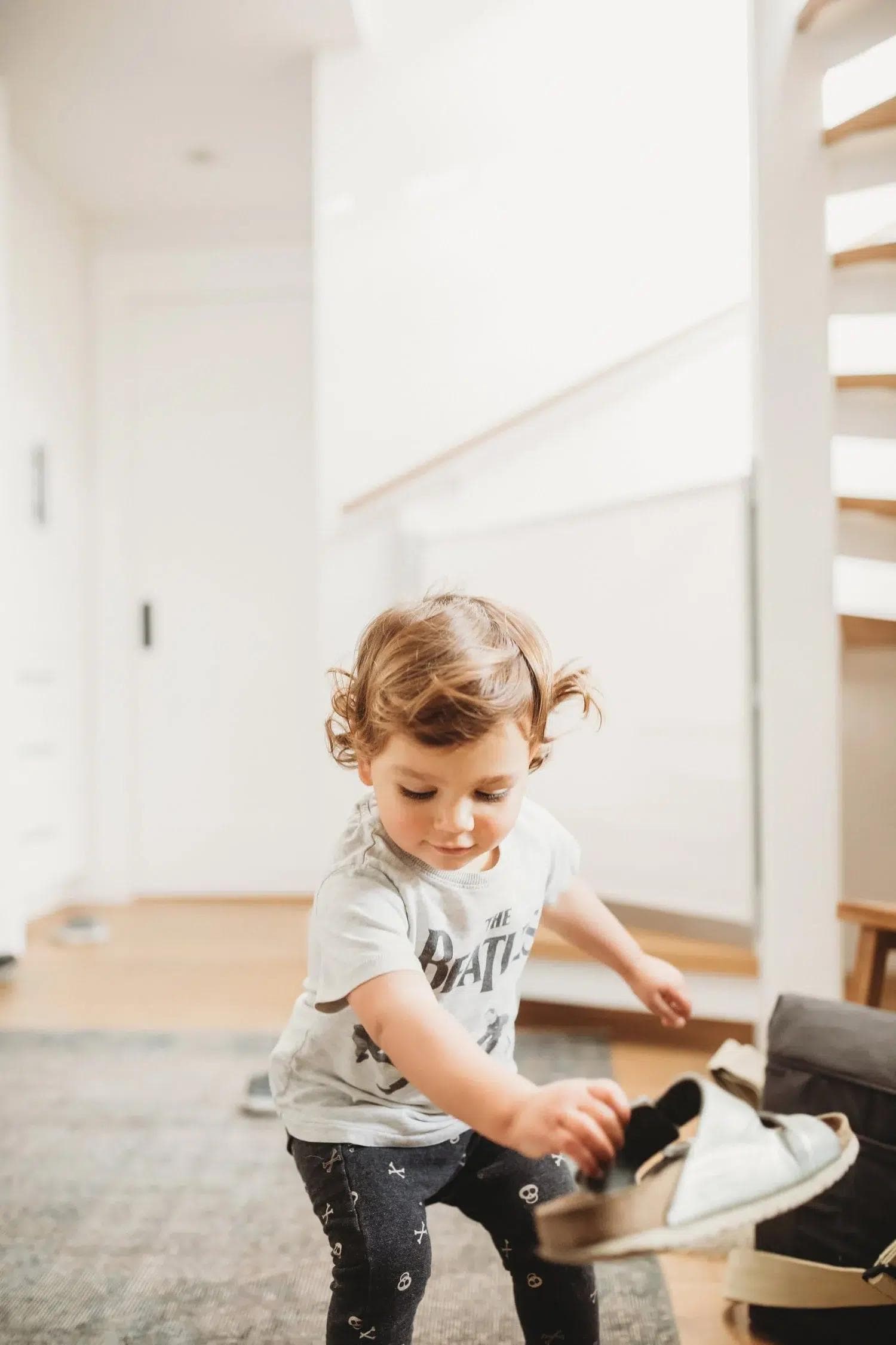 Toddler crouching to pick up a shoe in a sunlit hallway