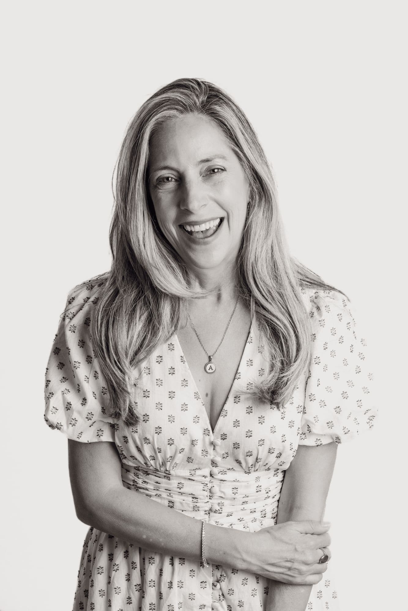 Black-and-white studio headshot of a woman in a floral dress, laughing