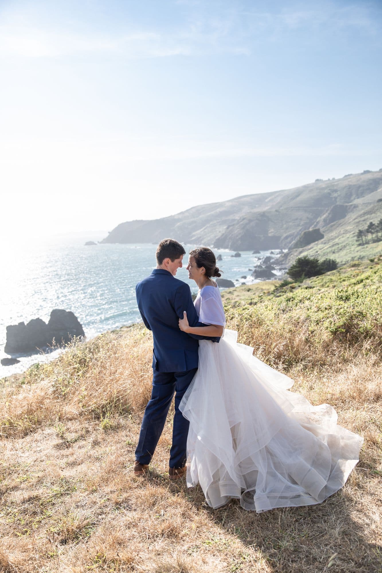 Bride and groom on a coastal bluff looking out over the Pacific