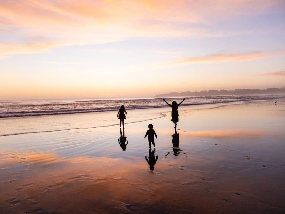 Three children silhouetted against a pastel sunset at the water's edge