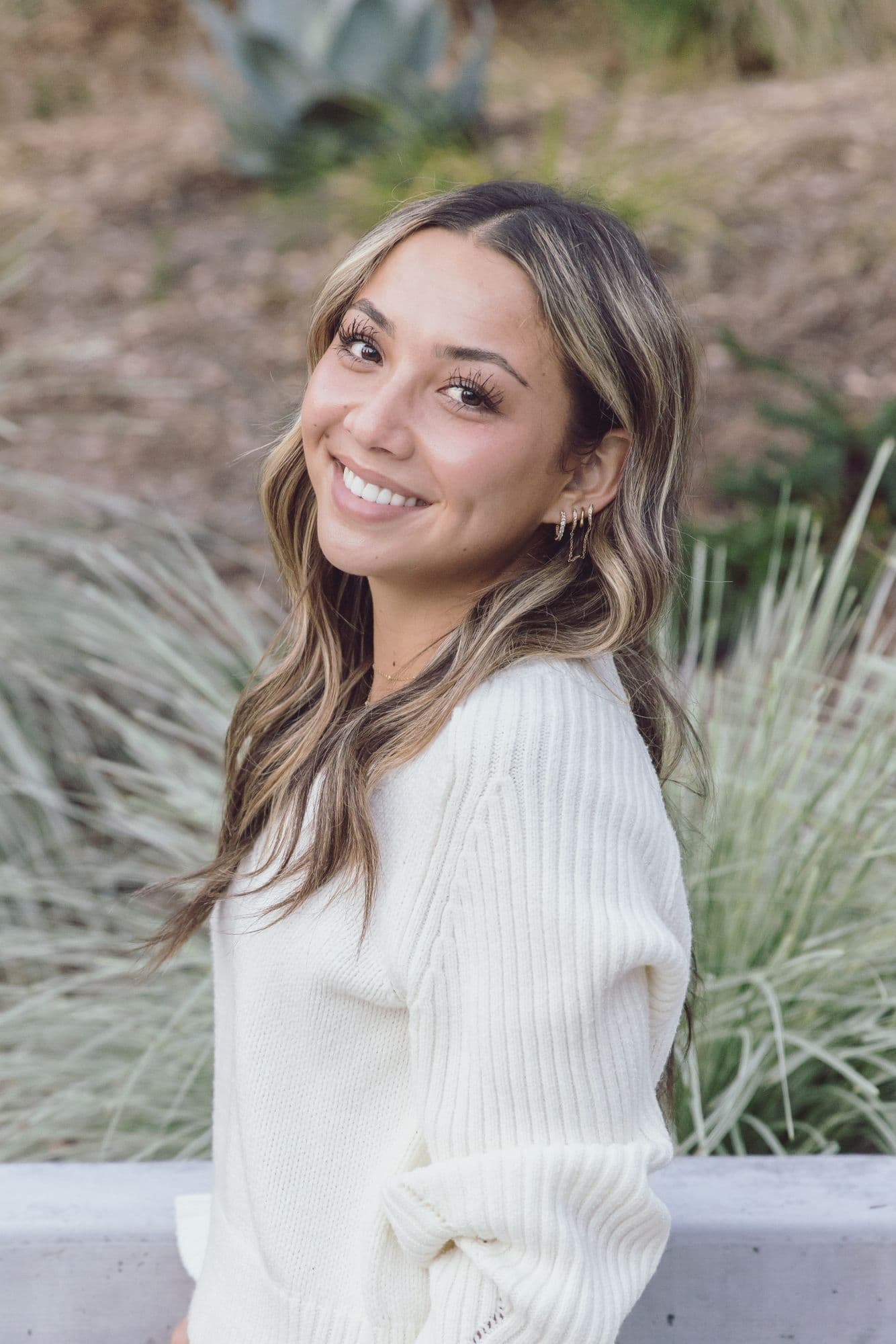 Outdoor headshot of a woman in a cream sweater beside ornamental grasses