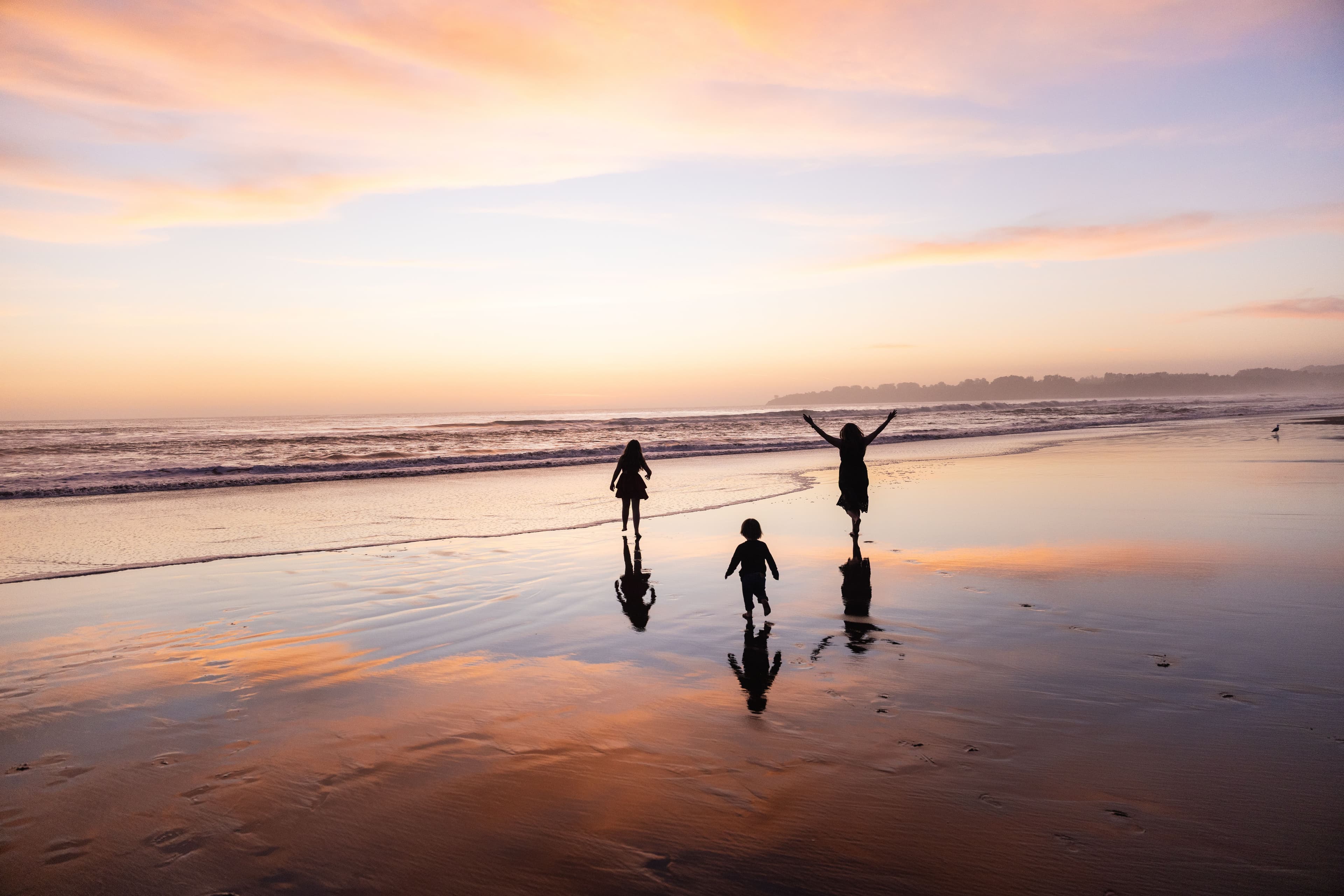 Children playing in the shallows at Stinson Beach under a pink and gold sunset
