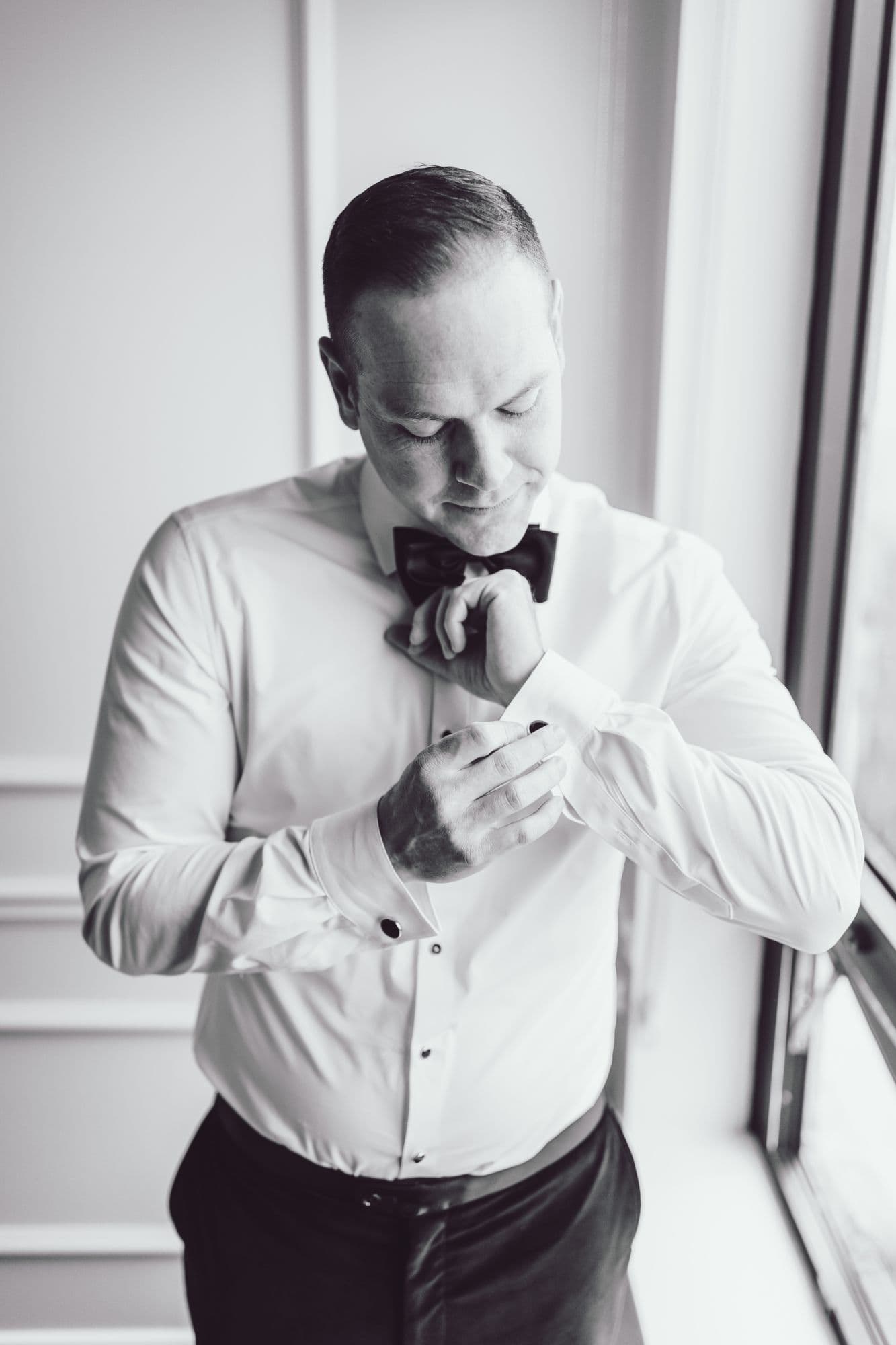 Groom fastening his cufflink by a window, black and white