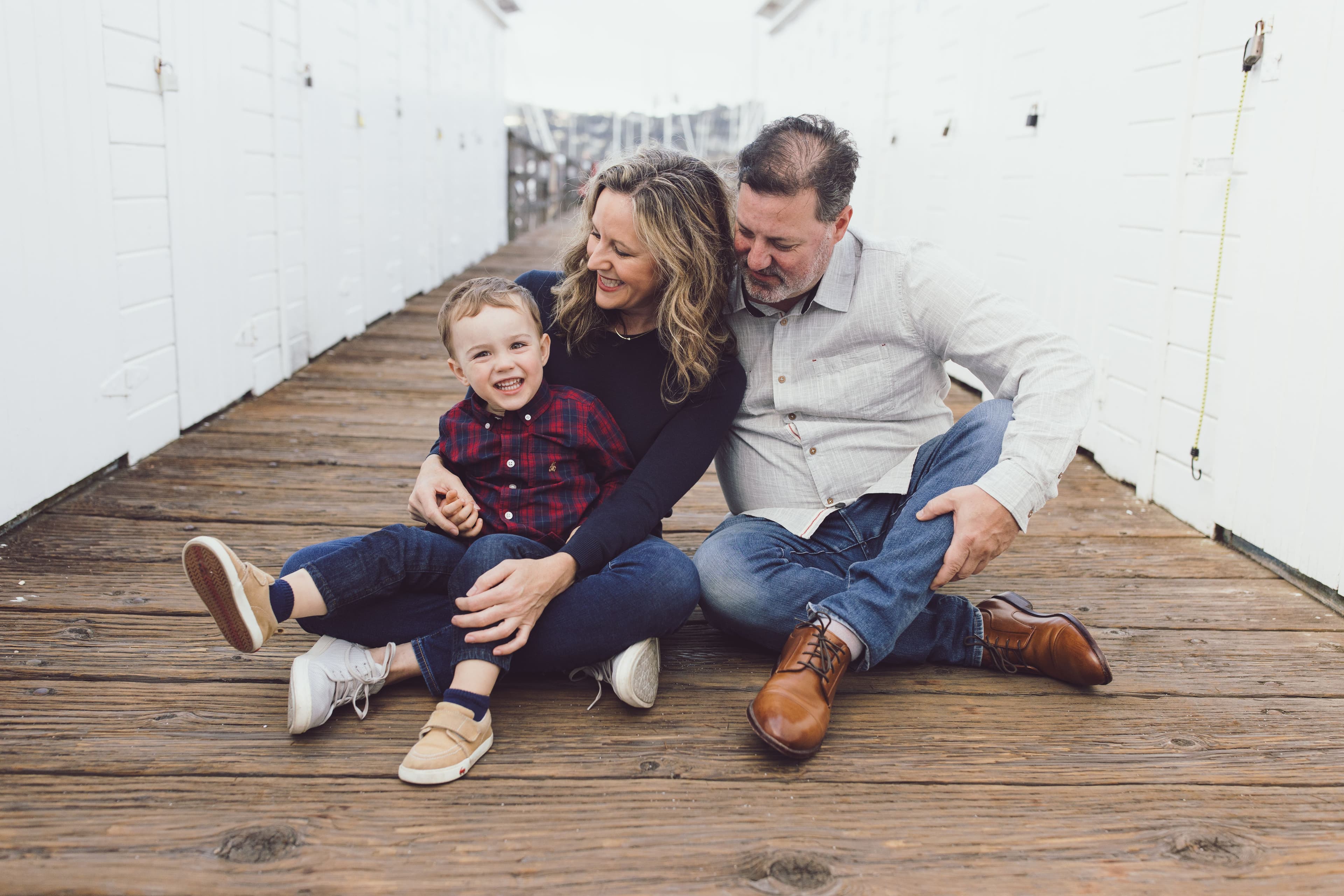 Family of three sitting together on a wooden pier