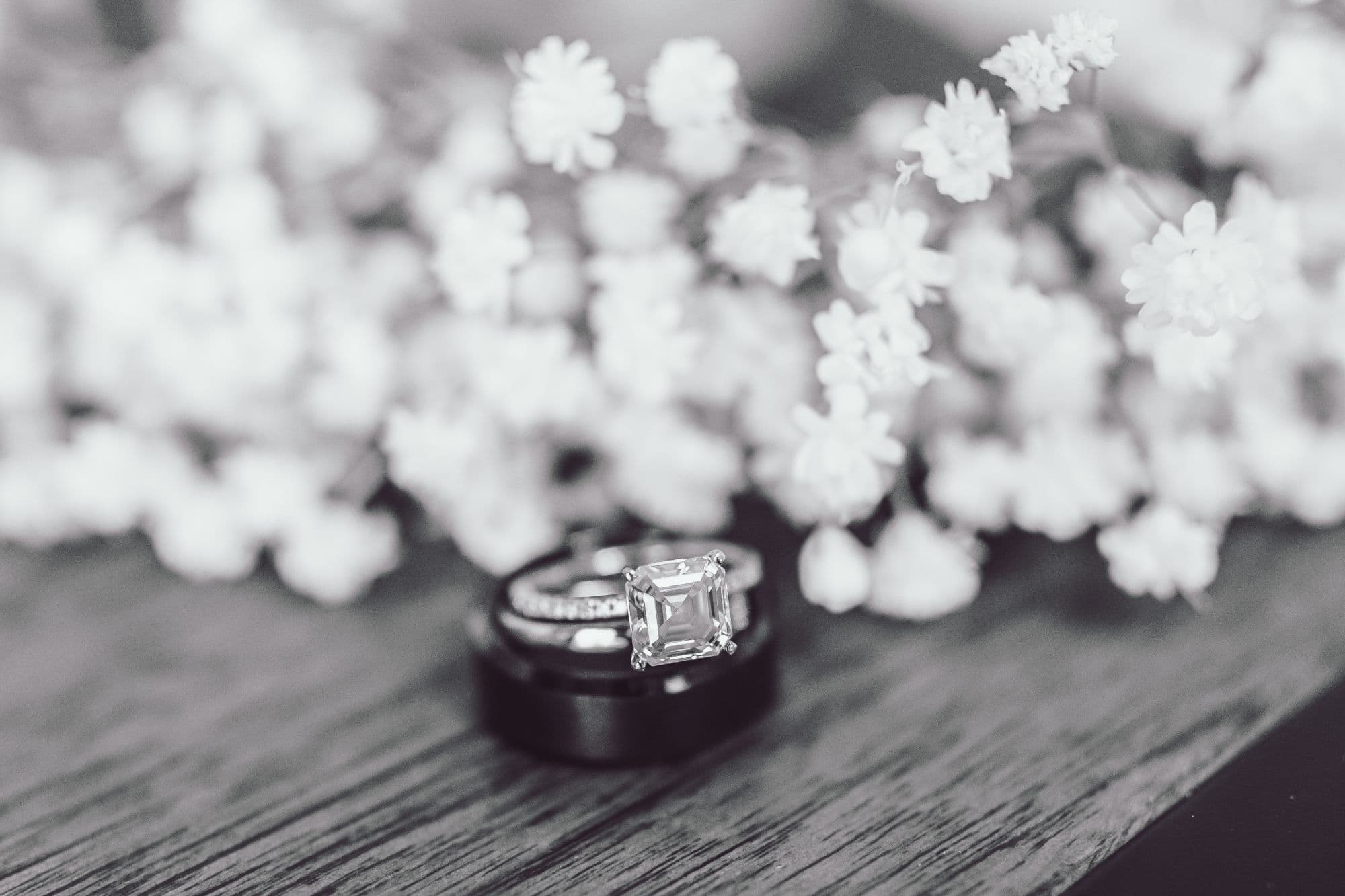 Engagement and wedding rings on weathered wood beside baby's breath, black and white