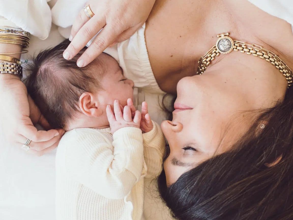 Mother and newborn lying face to face on white bedding