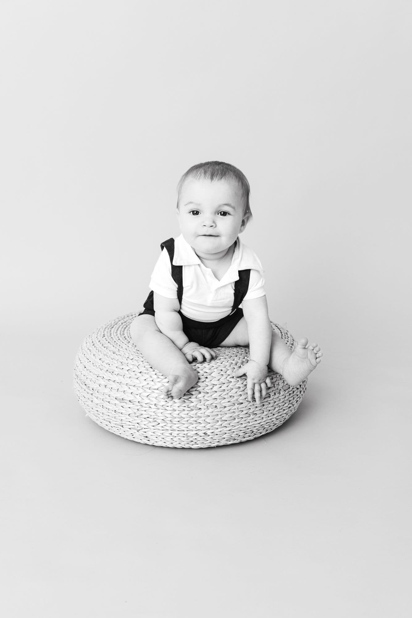Baby sitting on a knitted pouffe, black and white studio portrait