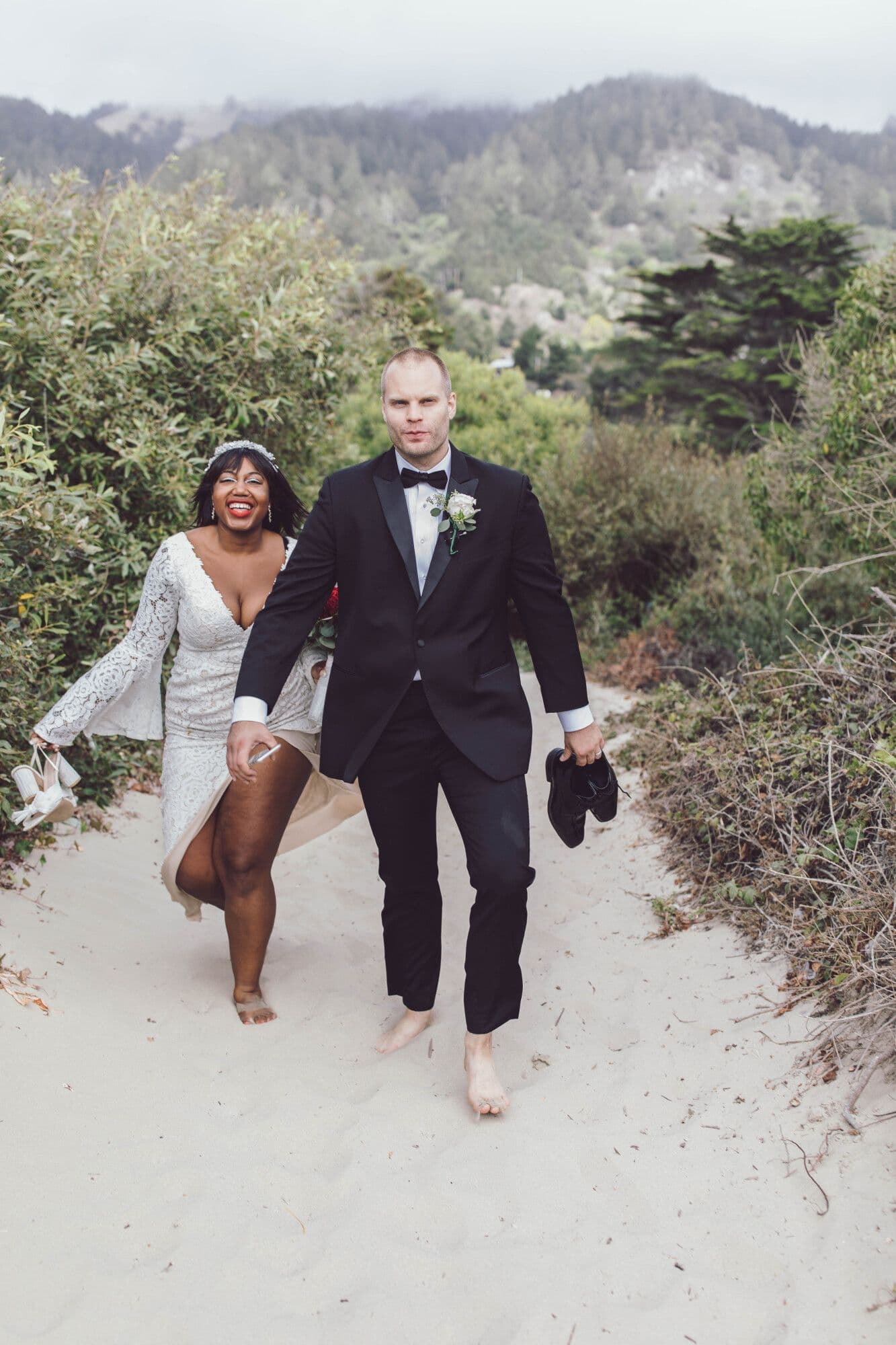Newlyweds walking barefoot through the dunes carrying their shoes