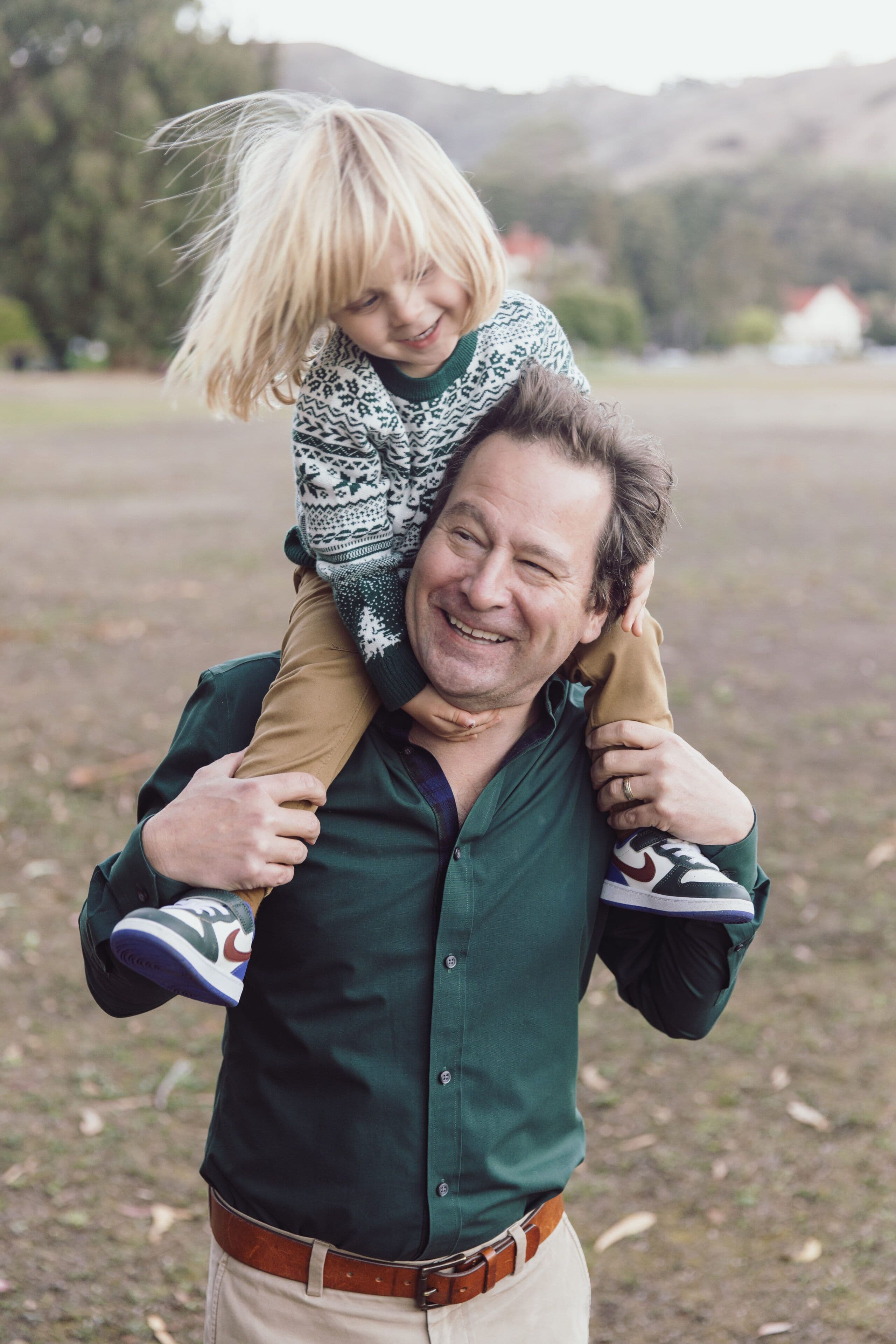 Father carrying his child on his shoulders across a grassy field