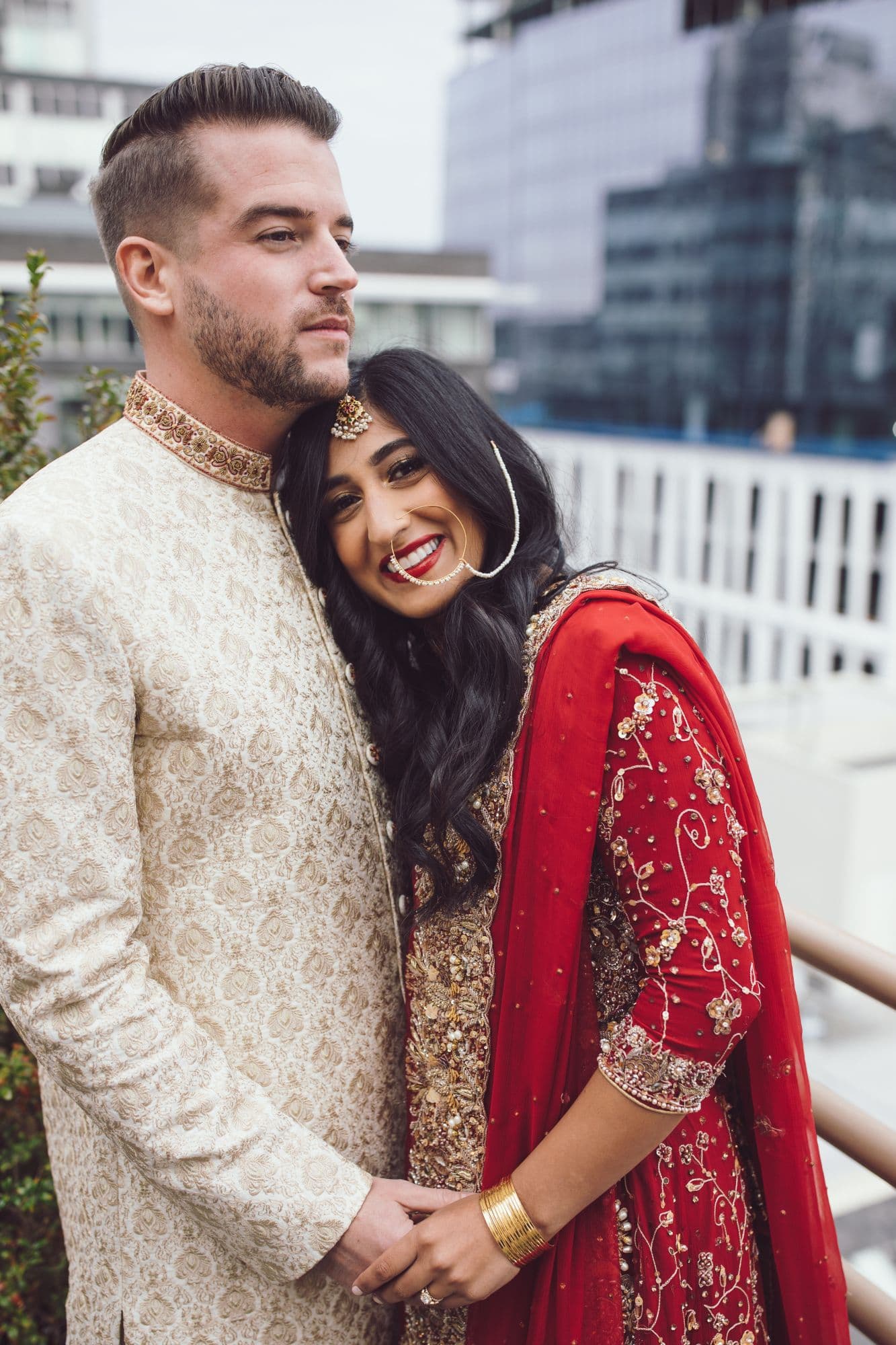 Couple in a sherwani and red lehenga holding hands on a rooftop