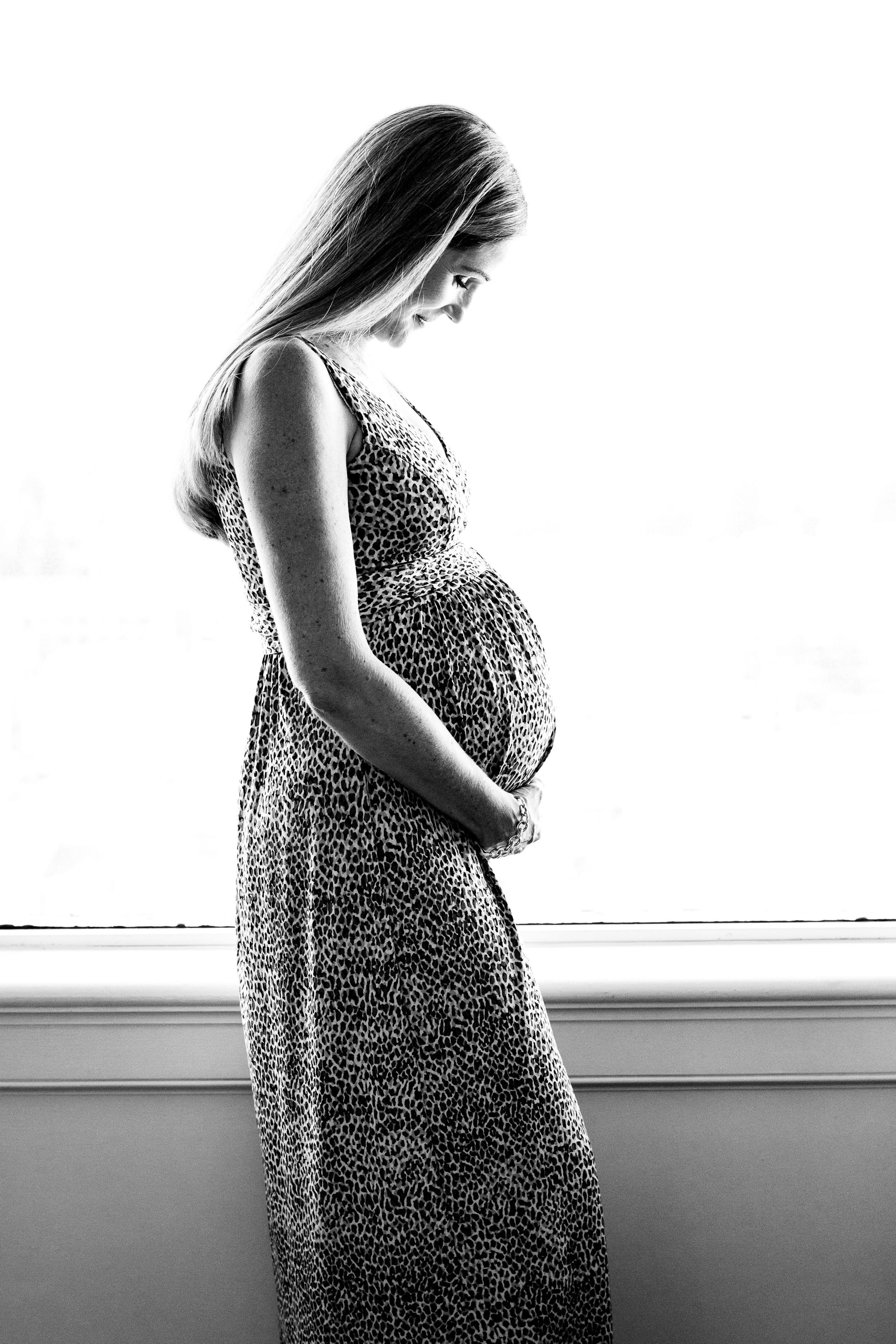 Expectant mother in profile at a window, hands resting on her bump, black and white