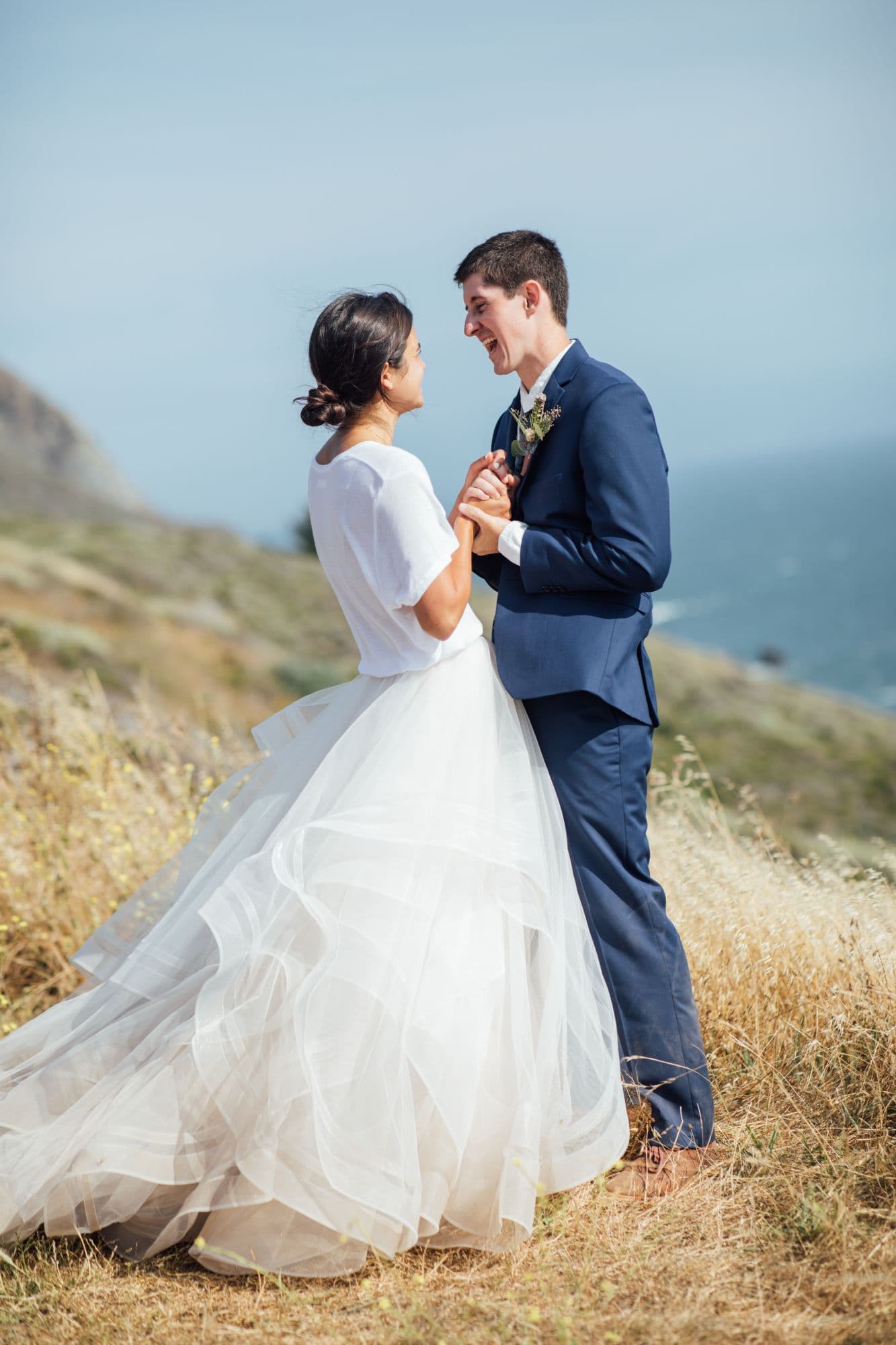 Bride and groom dancing together on a grassy bluff above the coast