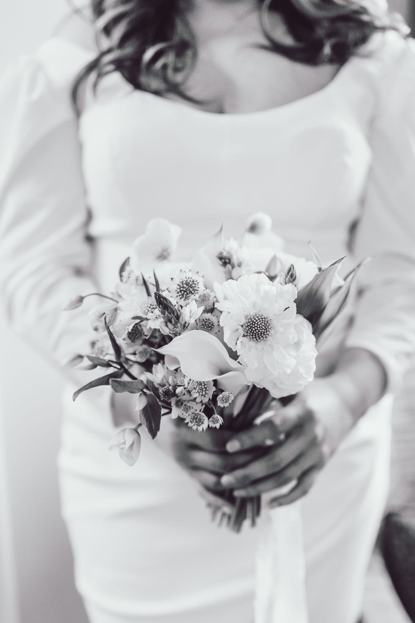 Bride's hands holding a white bouquet against a plain gown, black and white