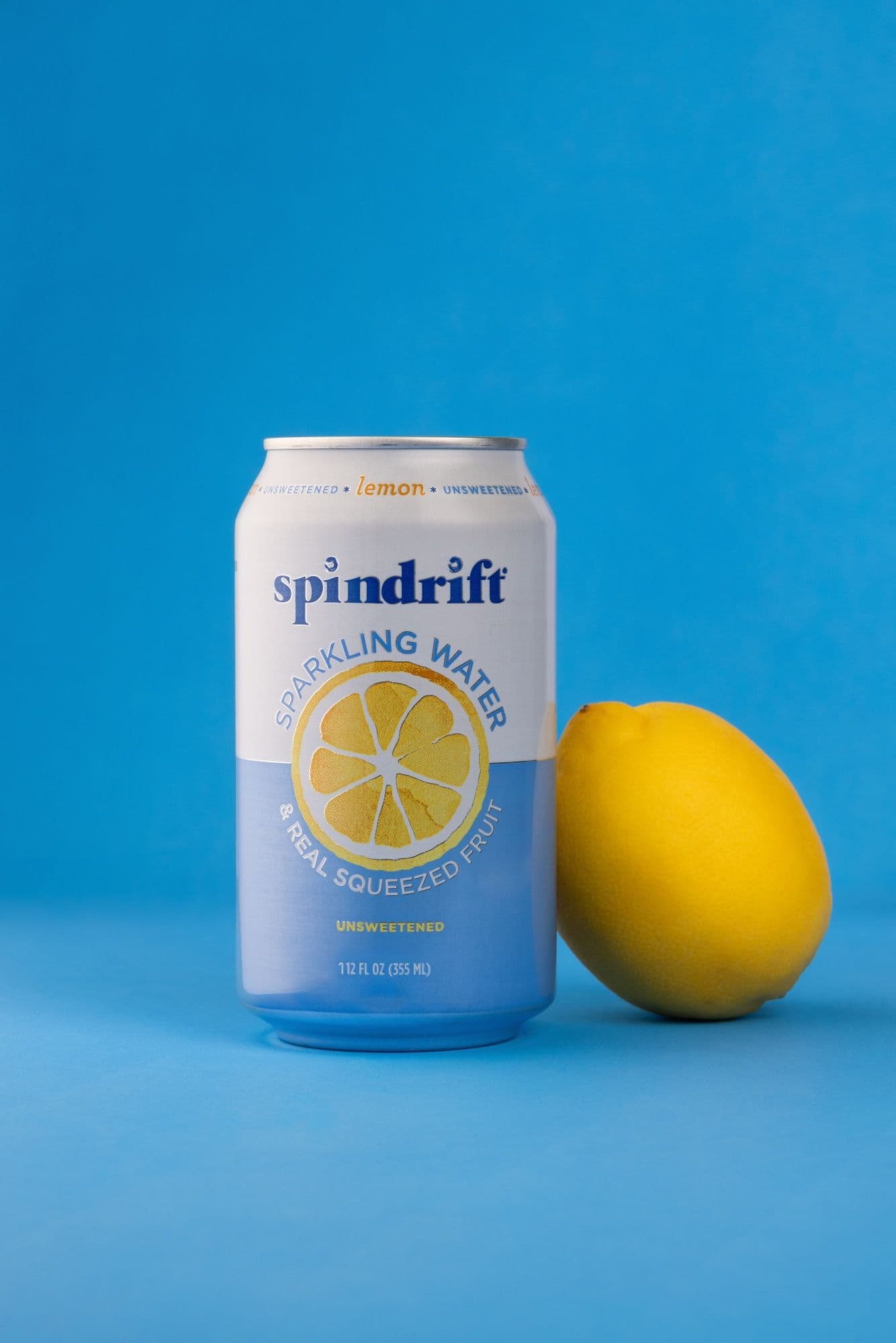 Can of Spindrift lemon sparkling water beside a whole lemon on a blue ground